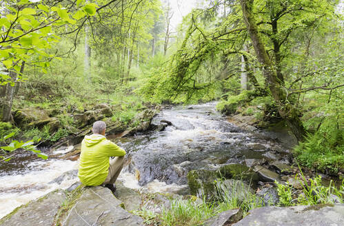 Mann sitzt auf einem Felsen und schaut auf die Rur, Naturpark Eifel, Monschau, Deutschland - GWF07334