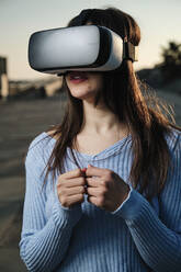 Young woman using virtual reality simulator at sunset - AGOF00229