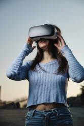 Young woman wearing virtual reality simulator at sunset - AGOF00230