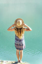 Frau mit Hut steht auf einem Felsen am See - OMIF00613
