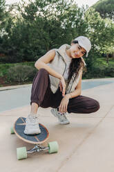 Smiling woman with skateboard on footpath in park - JRVF02741