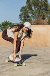 Smiling woman skateboarding in park on sunny day - JRVF02744