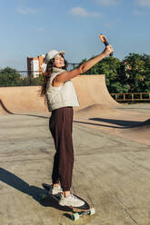 Young woman taking selfie on smart phone in skateboard park - JRVF02745