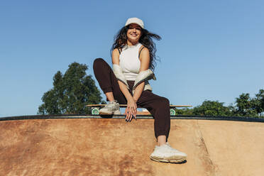 Lächelnde Frau im Skateboardpark an einem sonnigen Tag - JRVF02751