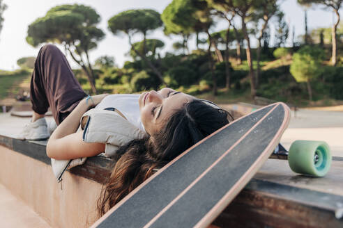 Frau liegt neben Skateboard im Park - JRVF02752