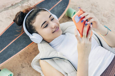 Frau mit Skateboard hört Musik über Kopfhörer und benutzt ihr Smartphone - JRVF02757