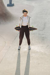 Lächelnde Frau mit Skateboard auf einer Sportrampe im Park - JRVF02760