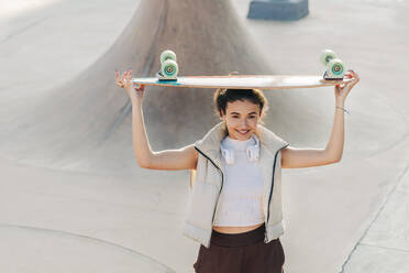 Frau hält Skateboard über Kopf im Park - JRVF02761