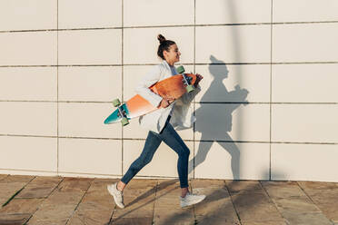 Young woman with skateboard running on footpath - JRVF02766