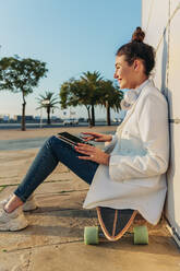 Lächelnde Frau mit Laptop auf Skateboard im Park sitzend - JRVF02775