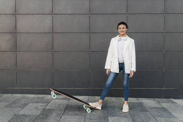 Lächelnde Frau mit Skateboard auf dem Fußweg - JRVF02781