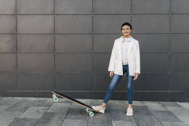 Smiling woman with skateboard on footpath - JRVF02781