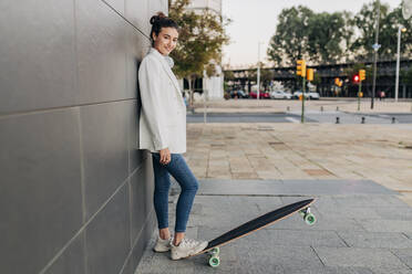 Lächelnde junge Frau mit Skateboard auf dem Fußweg - JRVF02782