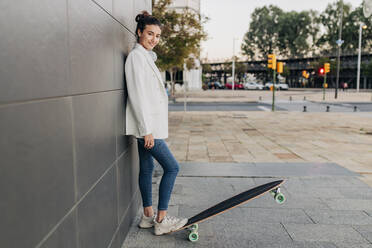 Smiling young woman with skateboard on footpath - JRVF02782