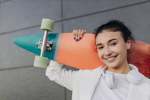 Lächelnde junge Frau mit mehrfarbigem Skateboard - JRVF02793