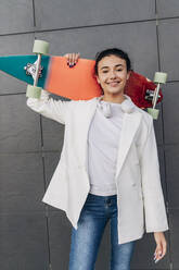 Junge Frau hält Skateboard vor einer Wand - JRVF02794