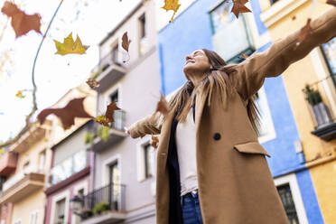 Woman with arms outstretched enjoying autumn leaves falling - XLGF02670