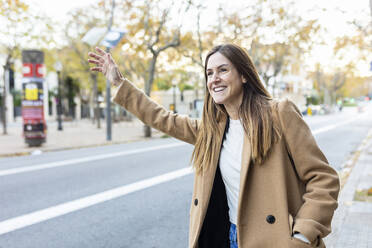 Happy woman hailing taxi on city street - XLGF02686