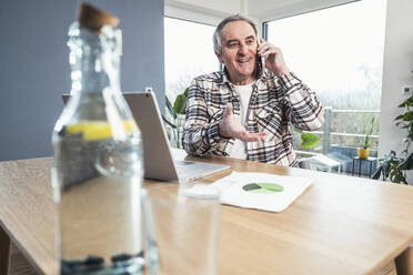 Smiling senior man talking on smart phone sitting at table - UUF25308