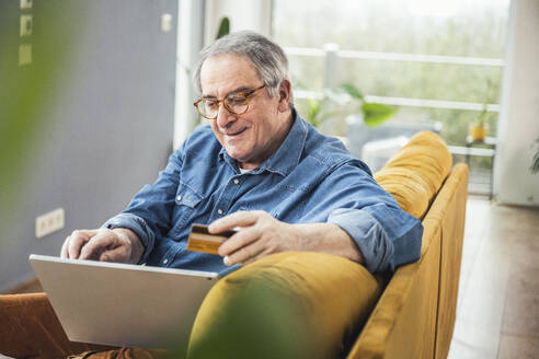 Senior man wearing eyeglasses making online payment through laptop at home - UUF25354