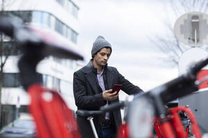 Mann benutzt sein Smartphone, um an einer Parkstation ein Fahrrad zu mieten - SGF02898