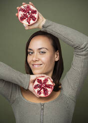 Frau hält halbierten Granatapfel vor grünem Hintergrund - JBYF00138