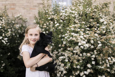 Blondes Mädchen mit Hund an weißer blühender Pflanze - ANF00012