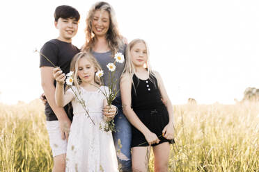 Mädchen hält Blumen mit Familie im Hintergrund auf einem Feld - ANF00017