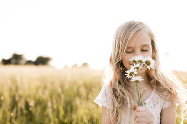 Blond girl smelling flowers in field - ANF00020