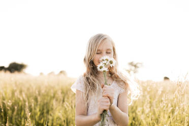 Cute girl smelling daisy flowers in field - ANF00021