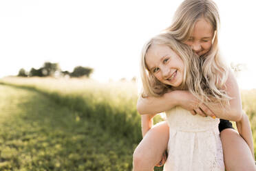 Smiling girl carrying sister piggyback at agricultural field - ANF00024