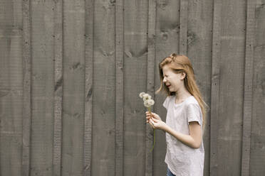 Girl with eyes closed holding dandelions by wall - ANF00051