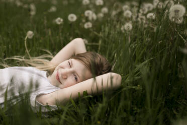 Cute girl winking and lying on dandelions in field - ANF00055