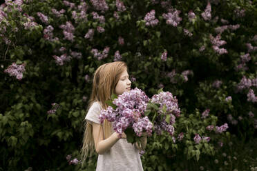 Blond girl with eyes closed holding lilac flowers in nature - ANF00062