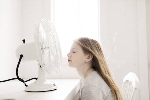 Girl sitting in front of table with electric fan at home - ANF00066