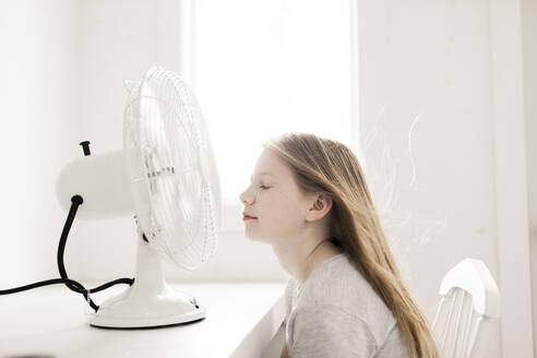 Mädchen sitzt vor einem Tisch mit elektrischem Ventilator zu Hause - ANF00066