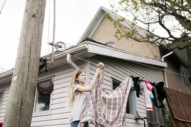 Mädchen hängt Kleidung an einem Seil vor dem Haus auf - ANF00069