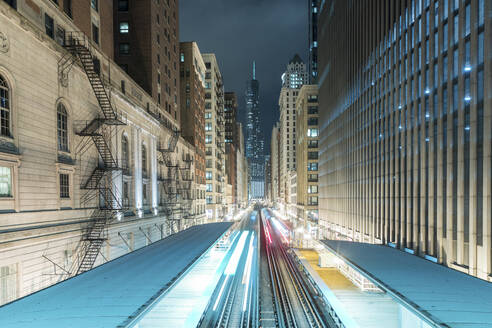 Light trails on railroad tracks amidst buildings in city at night, Chicago, USA - WPEF05780