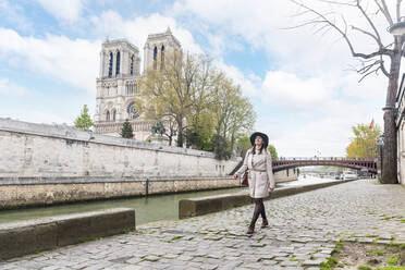 Frau, die im Urlaub am Fluss mit der Kathedrale Notre Dame im Hintergrund spazieren geht - WPEF05798