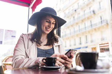 Glückliche junge Frau mit Smartphone in einem Café, Paris, Frankreich - WPEF05803