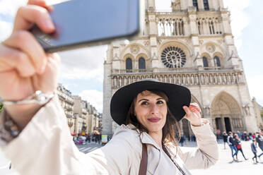 Junge Frau macht Selfie auf Smartphone mit der Kathedrale Notre Dame - WPEF05804