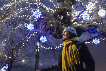 Woman wearing yellow scarf standing under illuminated tree - MTBF01143