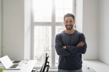 Smiling businessman with arms crossed in office - DIGF17444