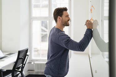 Smiling businessman writing on adhesive note in office - DIGF17447