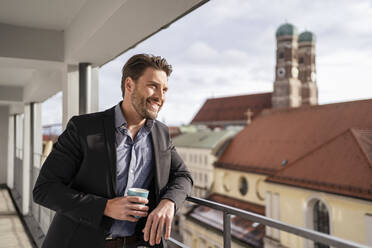 Smiling businessman with coffee cup on office balcony - DIGF17451