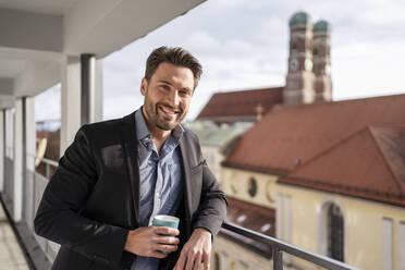 Lächelnder Geschäftsmann mit Kaffeetasse auf dem Balkon stehend - DIGF17452