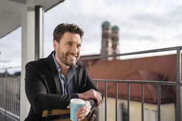 Glücklicher Geschäftsmann mit Kaffeetasse auf dem Bürobalkon - DIGF17453