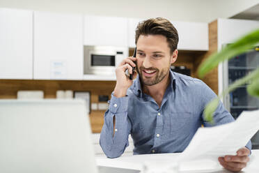 Geschäftsmann, der mit seinem Smartphone telefoniert und einen Laptop im Büro benutzt - DIGF17460