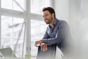 Contemplative businessman leaning on chair at office - DIGF17467