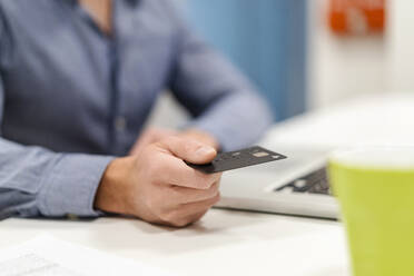 Businessman with credit card by laptop at desk in office - DIGF17476